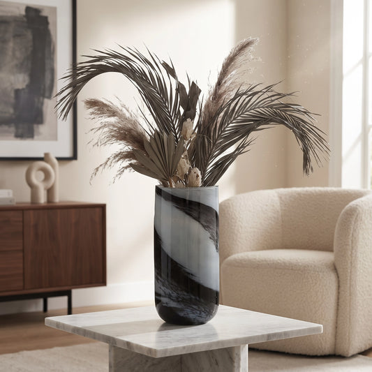 Grey and black decorative glass vase with dark dried foliage displayed on a marble side table