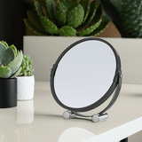 Grey shaving mirror with feet on bathroom vanity and plant reflection