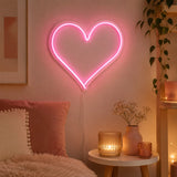 Pink heart LED neon light on bedroom wall beside bedside table with candles and plant