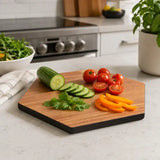 Hexagonal wooden cutting board with black edge displayed with sliced cucumber, tomatoes and peppers