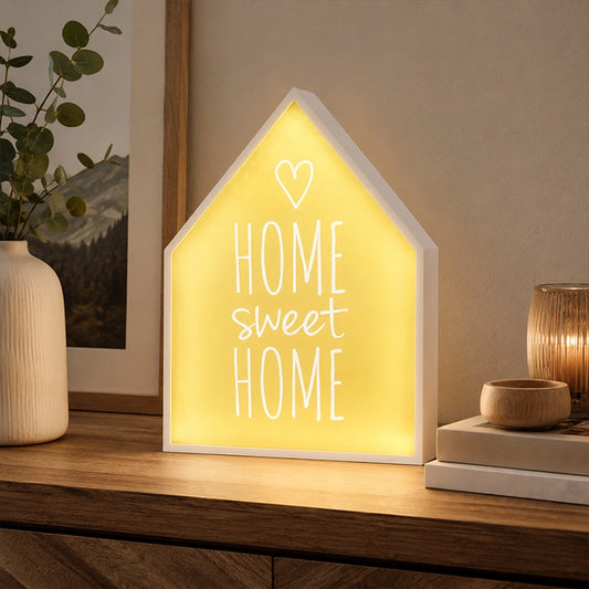 Home sweet home LED light box glowing on wooden sideboard beside vase and candles