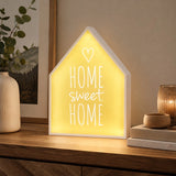 Home sweet home LED light box glowing on wooden sideboard beside vase and candles