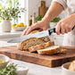 Black-handled kitchen knife slicing a loaf of fresh bread on a dark wooden cutting board