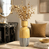 Large decorative vase with gold finish and black and white striped base holding dried foliage