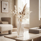 Large clear ribbed glass vase filled with dried botanical stems in a neutral living room