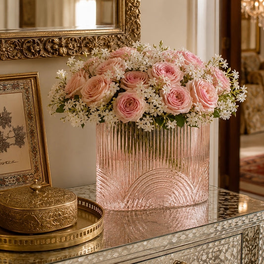 Large pink textured glass vase filled with soft pink and white flowers on a mirrored console table