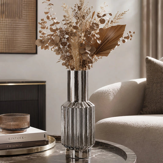 Large silver ribbed glass vase with dried botanical stems displayed on a coffee table