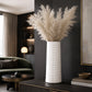 Large white cylindrical ceramic vase with subtle horizontal detailing and tall cream dried foliage on a dark console table