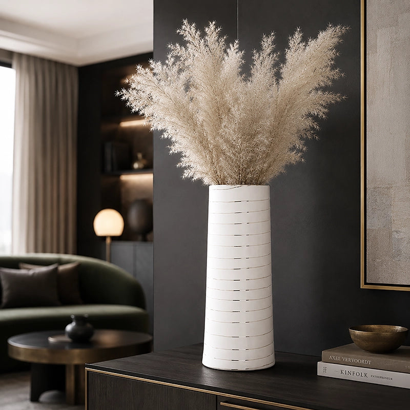 Large white cylindrical ceramic vase with subtle horizontal detailing and tall cream dried foliage on a dark console table