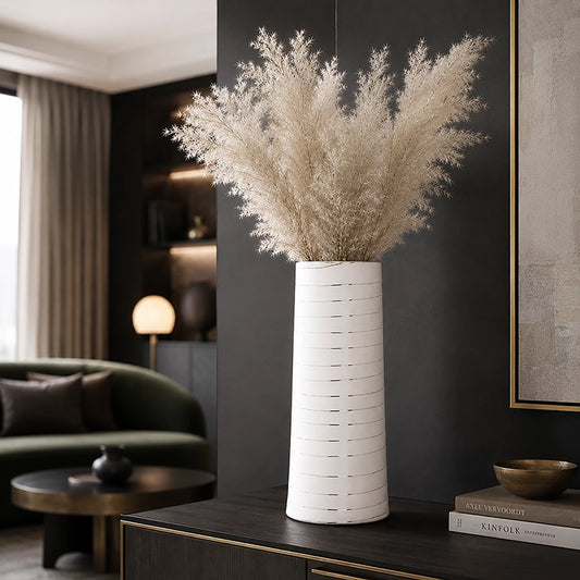 Large white cylindrical ceramic vase with subtle horizontal detailing and tall cream dried foliage on a dark console table