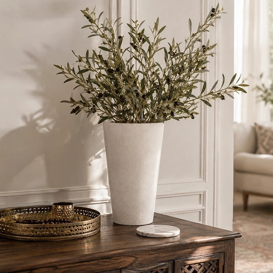 Large white tapered vase with tall leafy branches displayed on a dark wooden console table