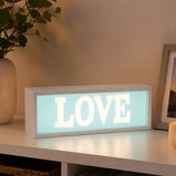 Love LED light box with glowing white letters on shelf beside plant and photo frame