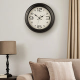 Matt black plastic wall clock above sofa with lamp in neutral living room