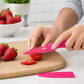 Pink ZING paring knife slicing fresh strawberries on a wooden chopping board with its blade cover beside it
