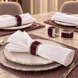 Purple napkin ring holding a white folded napkin beside a dark red table runner