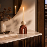 Red arch-shaped candle holder with white taper candle styled on a marble console table