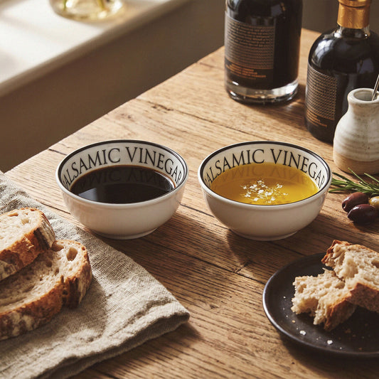 Two white balsamic dipping bowls filled with oil and vinegar served with bread on a wooden table