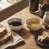 Two white balsamic dipping bowls filled with oil and vinegar served with bread on a wooden table