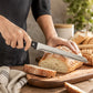 Silver serrated bread knife slicing a crusty loaf on a wooden chopping board