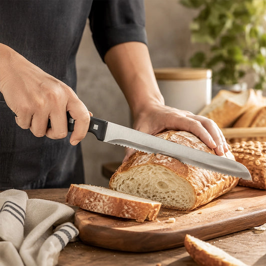 Silver serrated bread knife slicing a crusty loaf on a wooden chopping board