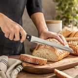 Silver serrated bread knife slicing a crusty loaf on a wooden chopping board