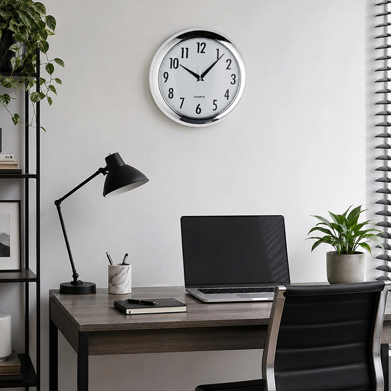 Silver plastic wall clock above home office desk with black lamp and laptop