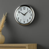Silver plastic wall clock with bold black numbers on grey wall