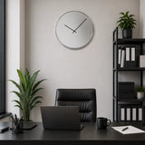 Silver wall clock above black office desk with shelving and plant