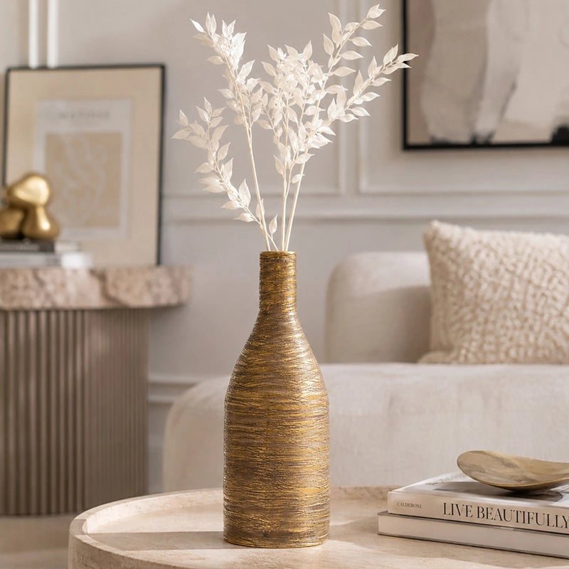 Small gold textured ceramic vase with white dried foliage displayed on a coffee table