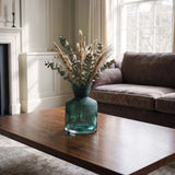 Small green glass vase with dried botanical stems displayed on a wooden coffee table