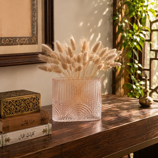 Small pink textured glass vase with dried bunny tail stems displayed on a wooden console table