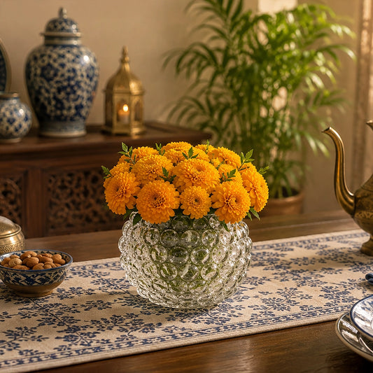 Small round textured glass vase filled with bright orange flowers on a dining table