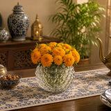 Small round textured glass vase filled with bright orange flowers on a dining table