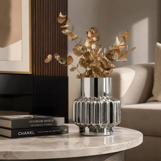 Small silver ribbed decorative vase with dried foliage styled on a marble coffee table