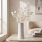 Small white ceramic vase with subtle line detail and decorative white dried stems