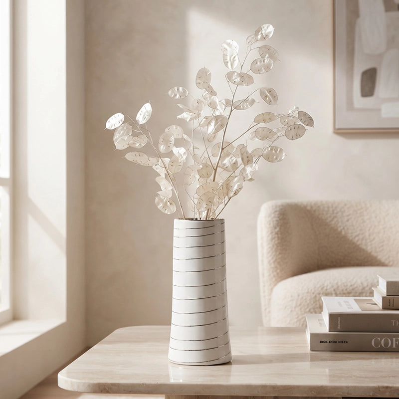 Small white ceramic vase with subtle line detail and decorative white dried stems