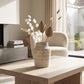 Small white textured ceramic vase with dried botanical stems styled on a wooden coffee table