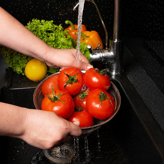 Stainless-steel mesh strainer rinsing fresh tomatoes under running kitchen tap water