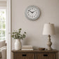 Vintage grey round wall clock above side table with lamp and vase