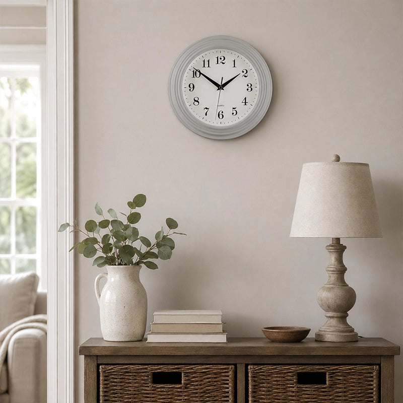 Vintage grey round wall clock above side table with lamp and vase