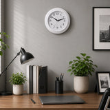 Vintage white wall clock above office desk with plants, books and black lamp