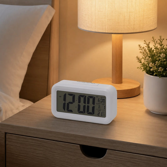 White digital alarm clock on dark bedside table with table lamp