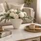 White round textured vase filled with white roses and eucalyptus on a marble coffee table