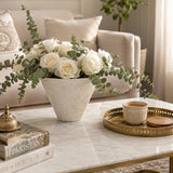 White round textured vase filled with white roses and eucalyptus on a marble coffee table