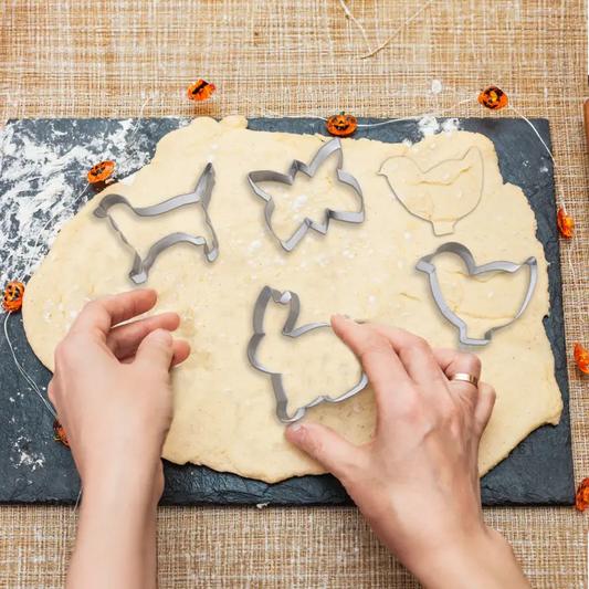 Hands cutting animal shape cookies from rolled dough with a metal cookie cutter set