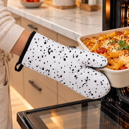 White oven glove with black splatter print gripping a white ceramic baking dish next to an open oven