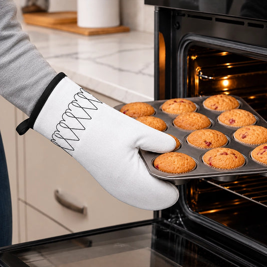 White single oven mitt with black geometric pattern used to remove a muffin tray from the oven