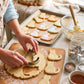 Hands cutting cat shaped cookies with a metal cat cookie cutter on a baking tray