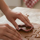 Hands pressing a gingerbread lady cookie cutter into rolled gingerbread dough