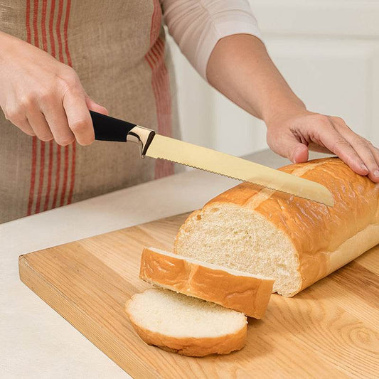 Gold serrated bread knife slicing a white loaf on a wooden chopping board